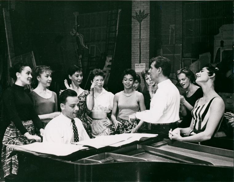 Stephen Sondheim on piano and Leonard Bernstein standing amongst female singers rehearsing for West Side Story
