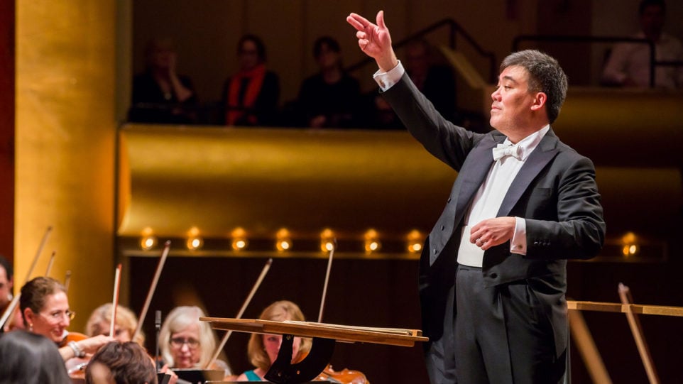 Alan Gilbert gestures towards musicians onstage