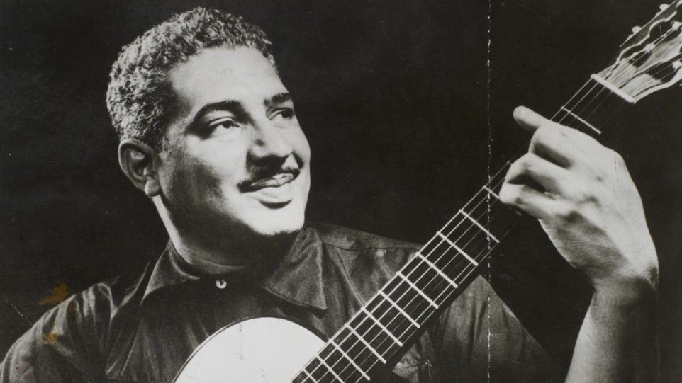 in a slightly weathered black and white photo, Dorival Caymmi strums a guitar