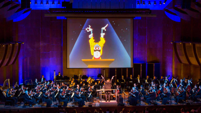 classical music orchestra onstage with Looney Tunes scene projected in background
