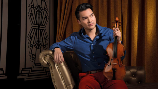 Hannu Lintu & Ray Chen seated in a luxurious chaise and holding a violin, Ray Chen looks into the distance