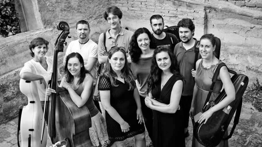 black and white group photo of musicians standing outside in front of a rustic wall