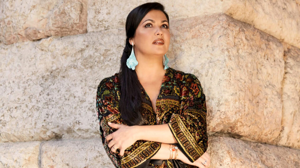 Woman in colorful robe and jade colored earrings against stone wall