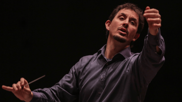 Portrait of Emanuele Andrizzi actively conducting, passionate expression, left hand gesturing, right hand holding baton