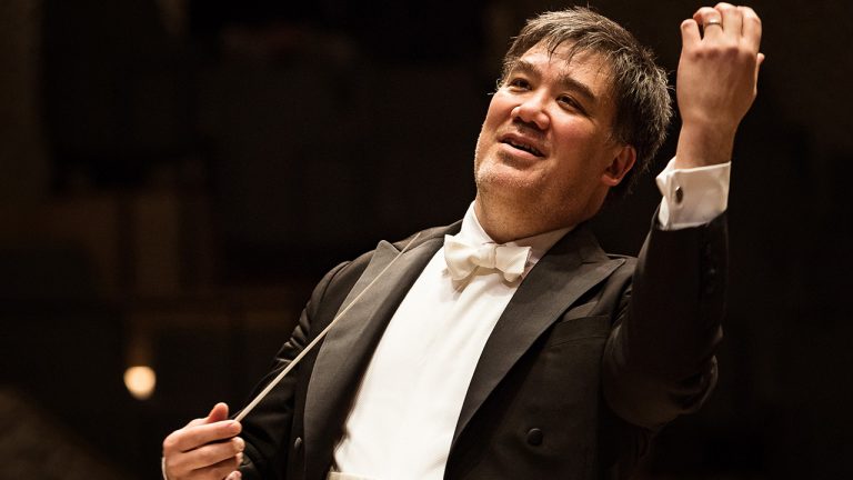 Alan Gilbert onstage, conducting with a slight smile