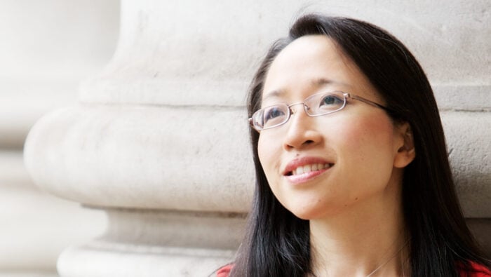 Portrait of Eugenia Cheng in front of bright stone building, looking into distance.