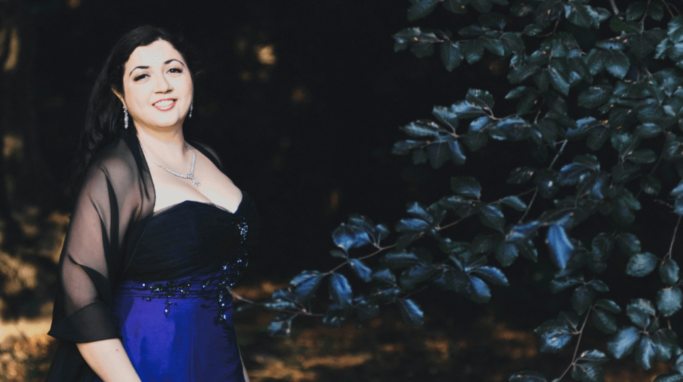 Portrait of Sherezade Panthaki in black and blue gown, organza wrap over shoulders, dark forest setting