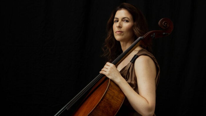 Woman sits with cello in front of dark background