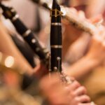 A close-up shot of a musician playing a black woodwind clarinet in an orchestra.