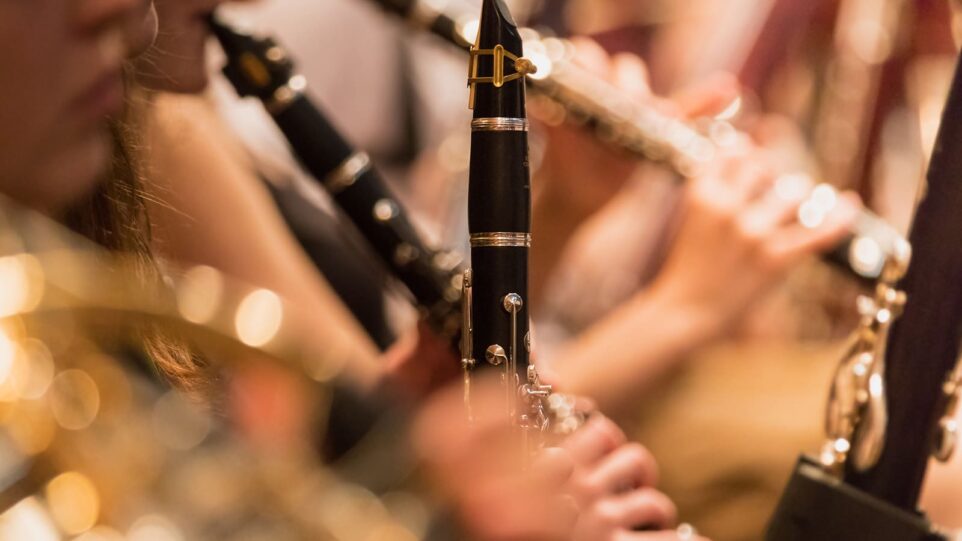 A close-up shot of a musician playing a black woodwind clarinet in an orchestra.