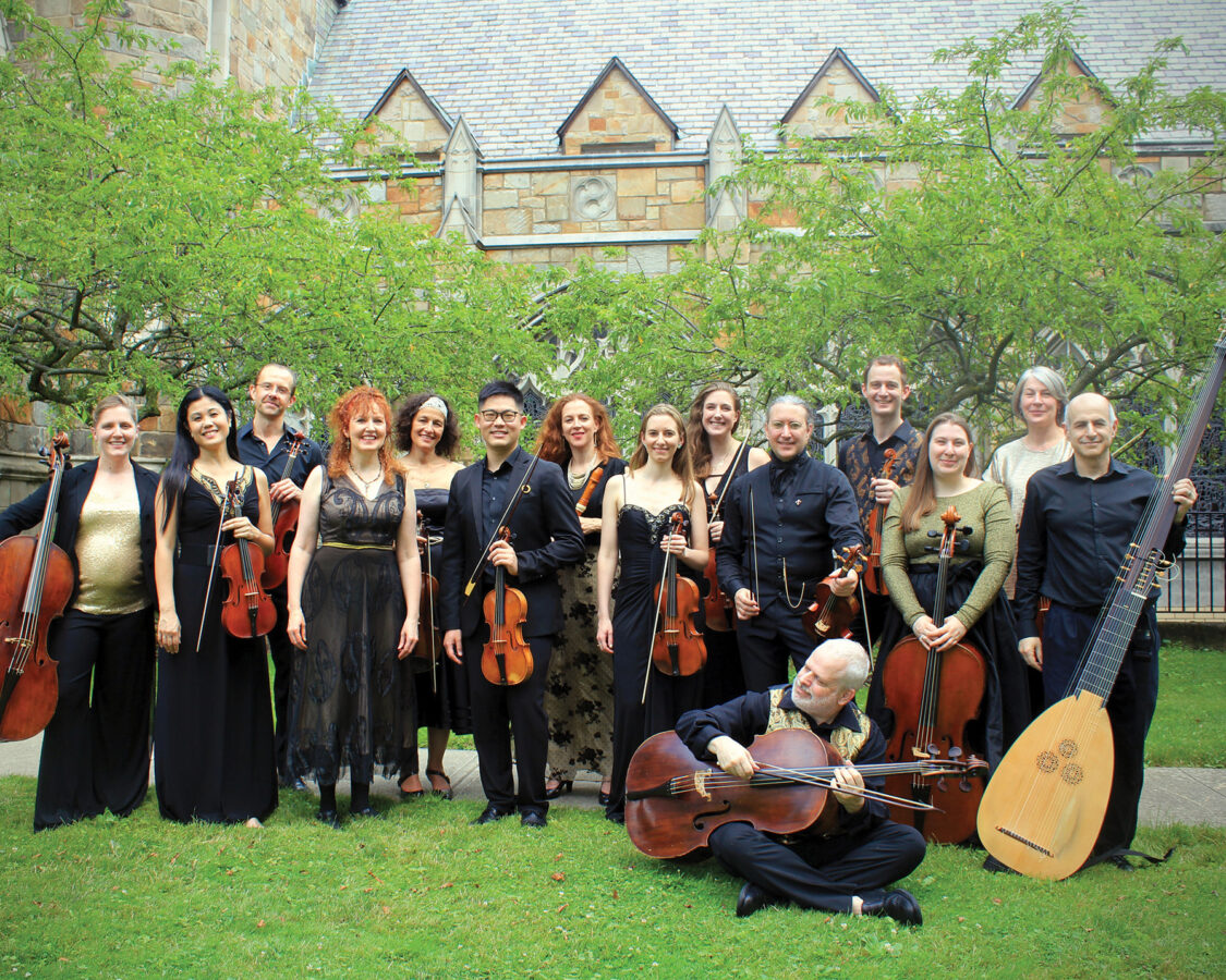 group of 15 musicians pose in verdant courtyard with period instruments