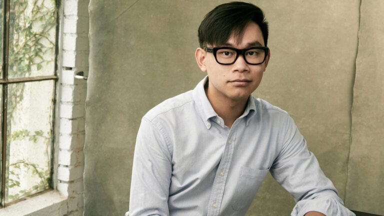 Composer Viet Cuong poses in front of a backdrop and a sunlit window