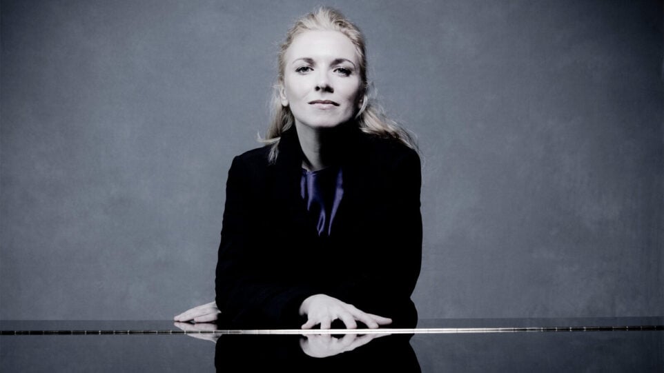 Tamara Stefanovich, in a black coat, seated at a closed piano