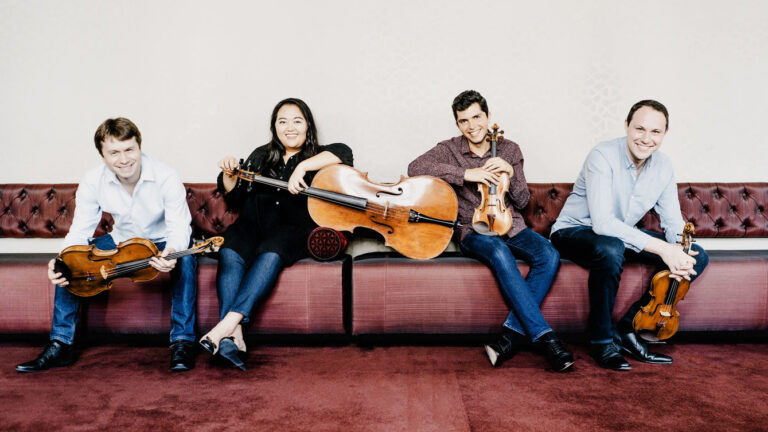 Calidore String Quartet poses casually on a red couch with instruments