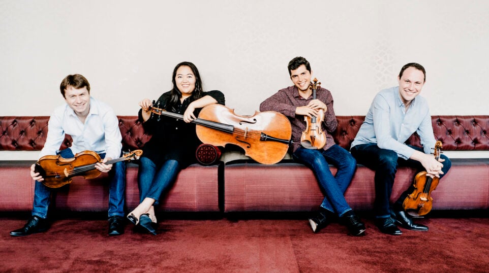 Calidore String Quartet poses casually on a red couch with instruments