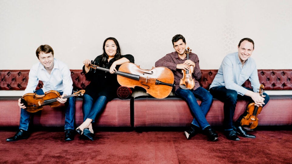 Calidore String Quartet poses casually on a red couch with instruments