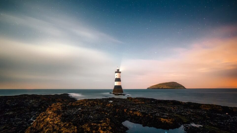 a striking lighthouse stands on a coastline against a cloudy, vivid sunset