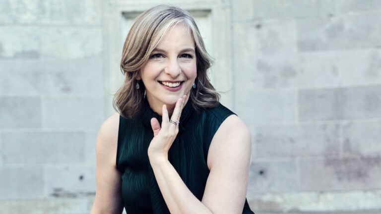 Portrait of Orli Shaham, smiling, in front of a light stone wall