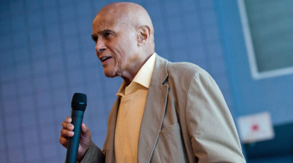 Harry Belafonte holds a microphone in front of a blue wall