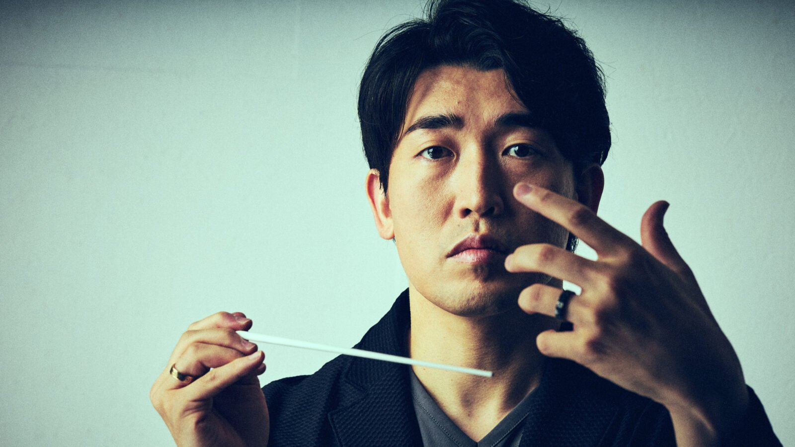Portrait of conductor Keitaro Harada, gazing at camera, holding a baton