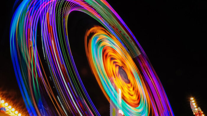 Bright, vibrant light trails of a ferris wheel in motion against a dark night sky