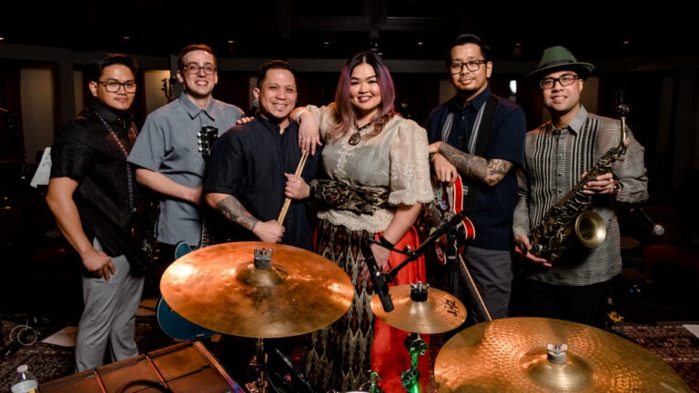 A group of musicians pose around a drumset