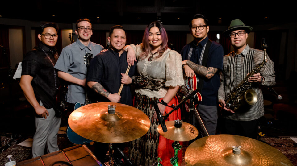 A group of musicians pose around a drumset