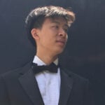 Samuel Lam wears a tux and poses outside against a black wall