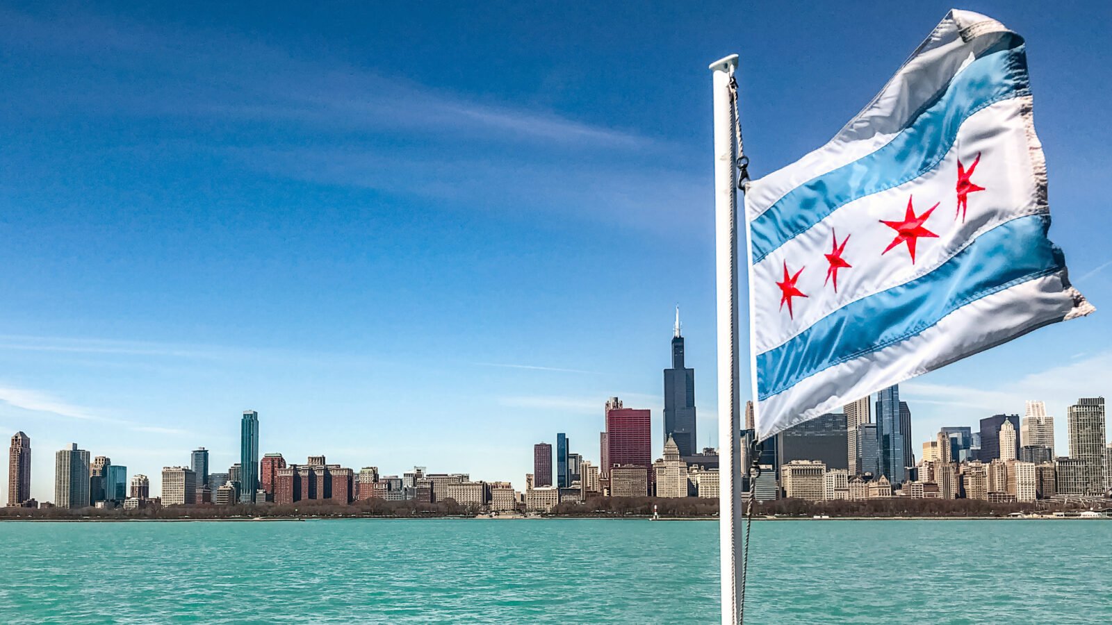 a chicago flag billowing in the wind, with a sunny view of the chicago skyline in the background