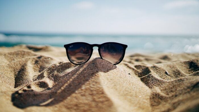 sunglasses sit on a sandy beach with water in the background