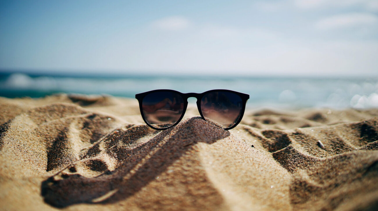 sunglasses sit on a sandy beach with water in the background