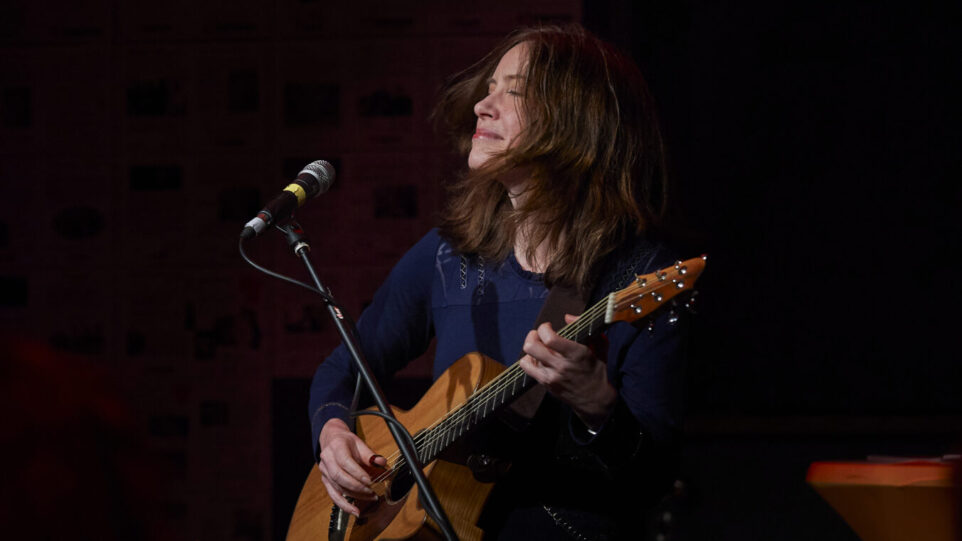 woman with closed eyes playing acoustic guitar