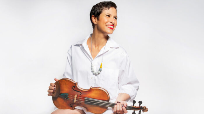 Elena Urioste seated, smiles while holding her violin