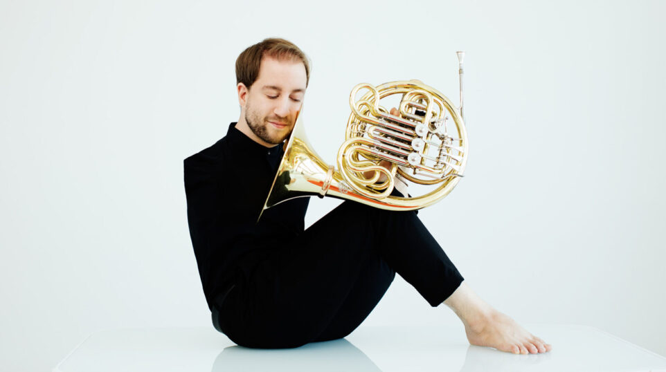 Felix Klieser, dressed in black, holds his French horn with his feet