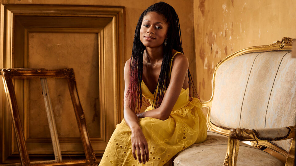 Isata Kanneh Mason, wearing gold, poses on a settee