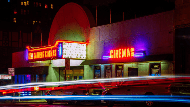 brightly lit movie theater marquee with car light streaks passing in front