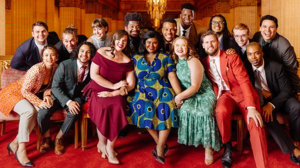 formally dressed artists pose together in a grand theater lobby