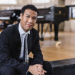 Clayton Stephenson sits with a piano in the background