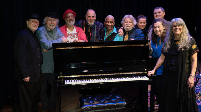 10 people standing behind upright piano