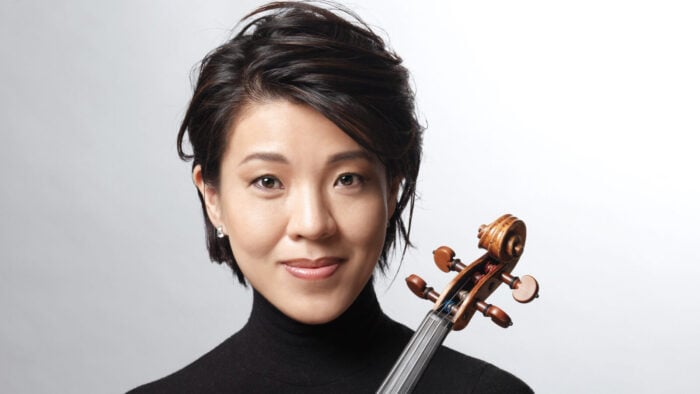 Kyoko Takezawa holds a violin in front of a white backdrop