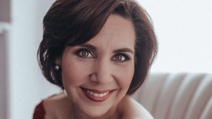 Jessica Rivera, wearing a red dress and pearl earrings, smiles