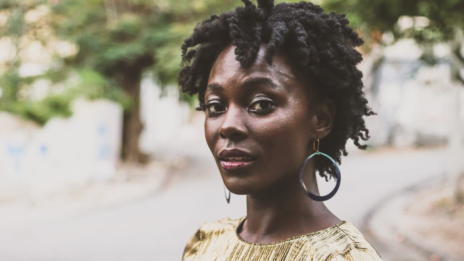 Nathalie Joachim poses on a street, trees in the background