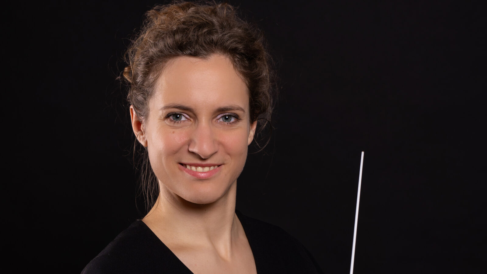 Taki Alsop Conducting Fellowship winnder Alena Hron holds a baton and poses against a black background