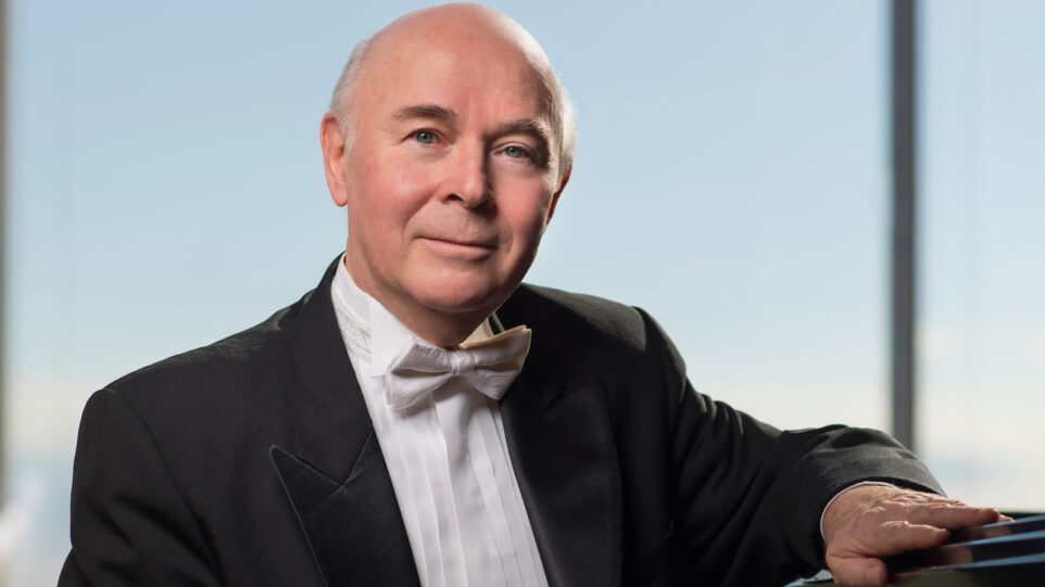 Jorge Federico Osorio gives a soft smile at a piano in front a big blue sky.