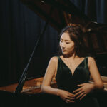 Wynona Wang leans against a moodily lit grand piano