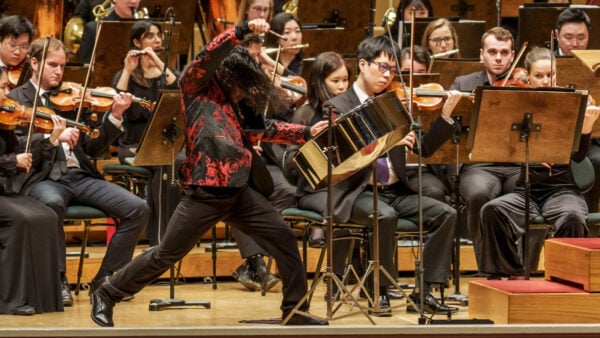 Clad in a patterned red-black suitcoat, Jaden Teague-Núñez strikes the steelpan with dynamism and athleticism