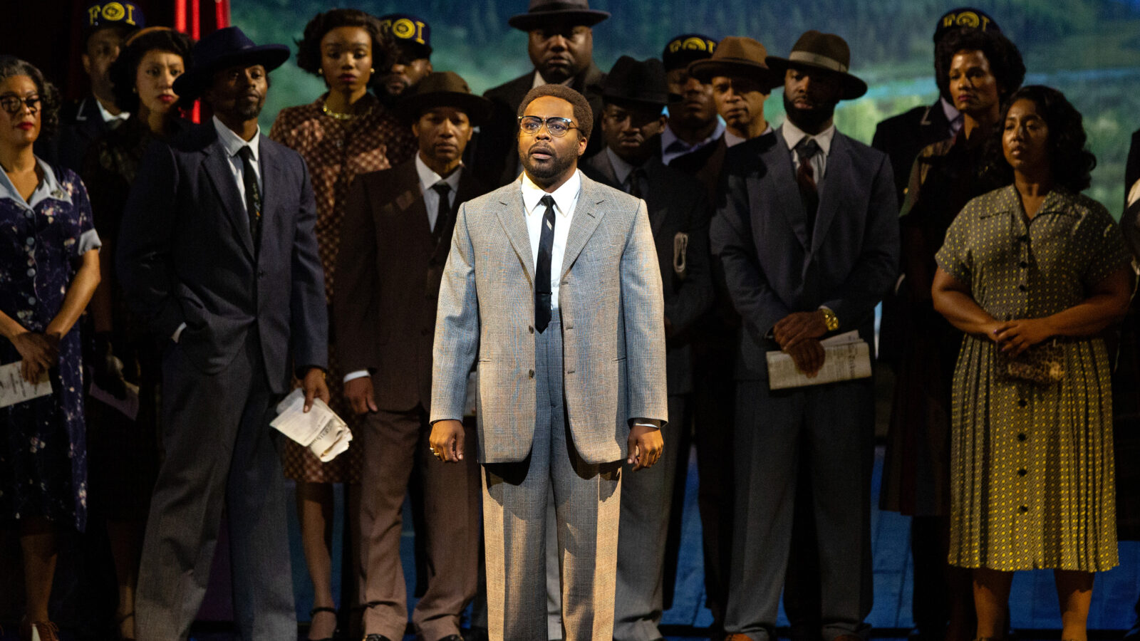 Will Liverman stands center stage dressed as Malcolm in a performance of "X: The Life and Times of Malcolm X"