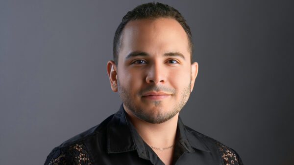 Studio portrait of Samuel Vargas wearing a heart necklace and a satin and lace black shirt