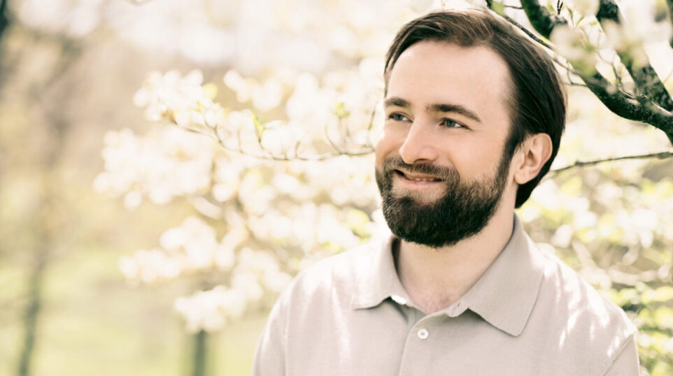 Daniil Trifonov smiles while under a sunlit tree