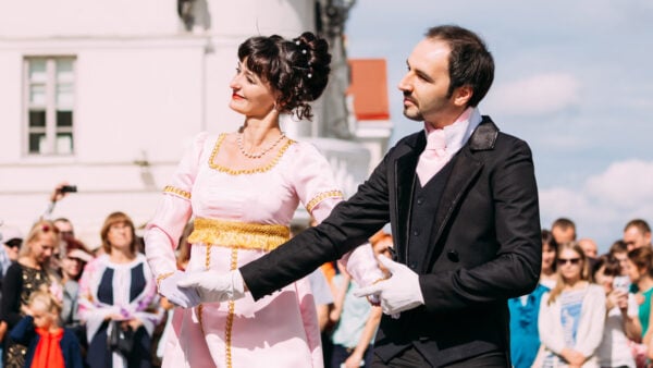 two young people in historic dress perform a traditional dance on a sunny day